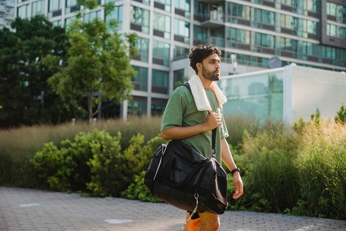Man with a gym bag and towel strolling in a park.