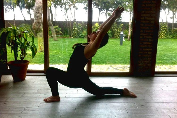 Person doing a yoga lunge inside near a large window.